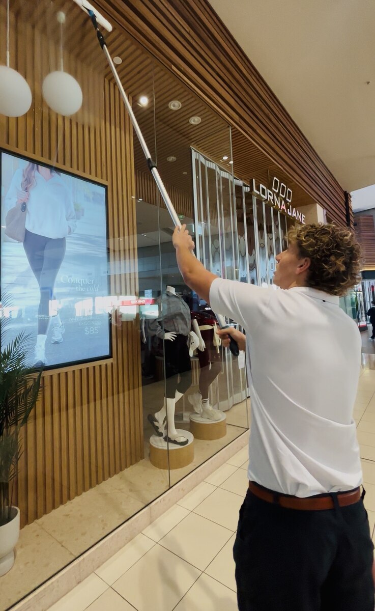 Luck's Cleaning Services technician cleaning a storefront window with an extension pole